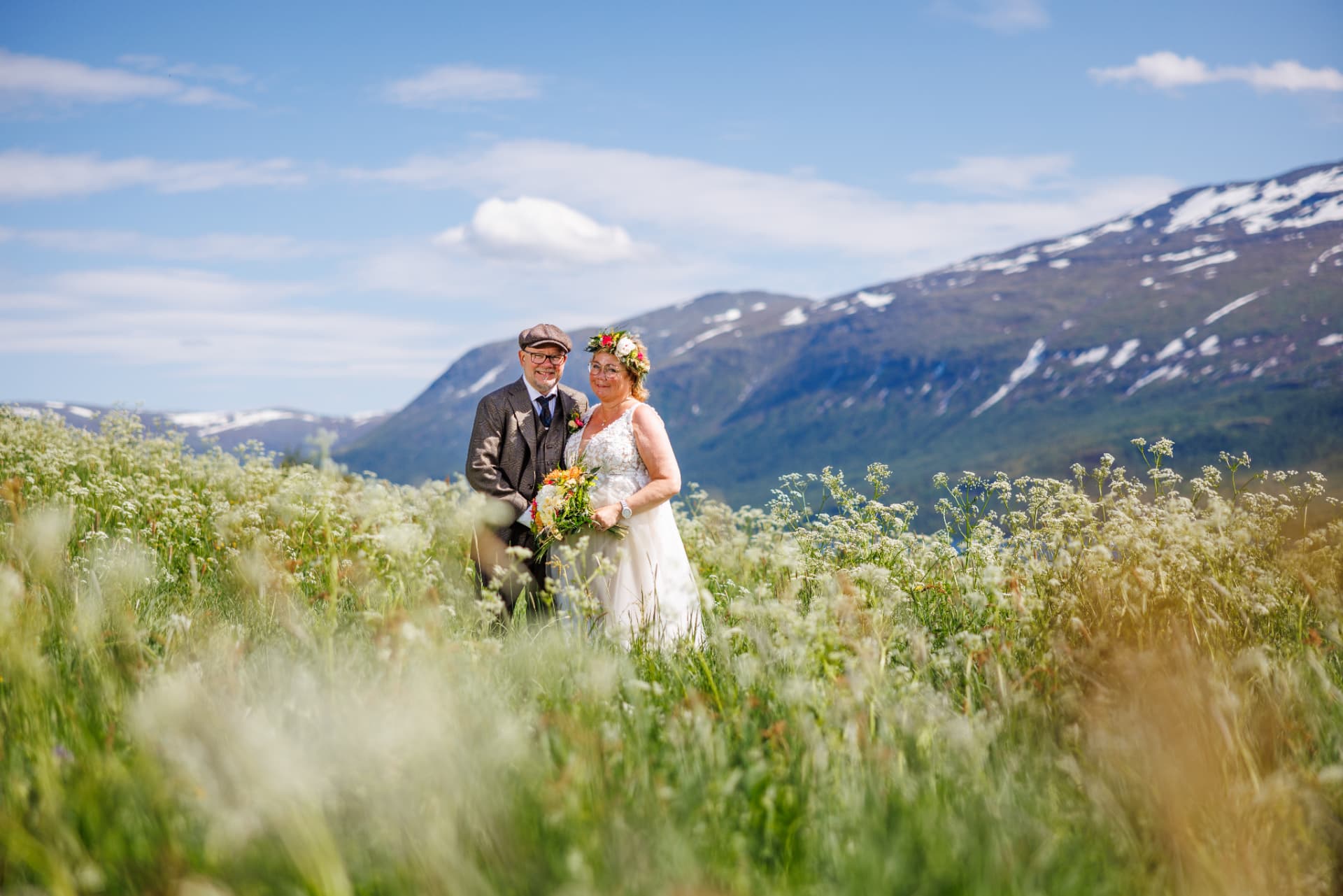 Brudepar i blomstereng med fjell i bakgrunnen
